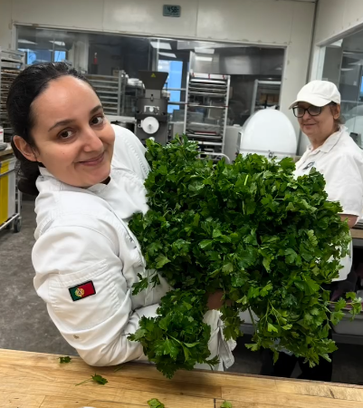 Karina, founder of Backyard Bakery, holding fresh parsley in a professional Miami bakery kitchen